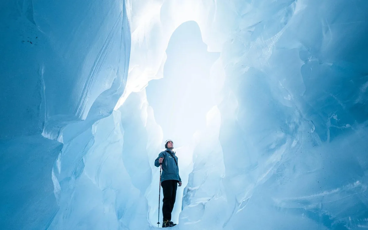 A hiker inside a blue ice tunnel on Franz Josef Glacier