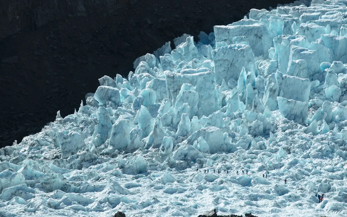 Tiny figures walking below the icefall of Franz Josef Glacier