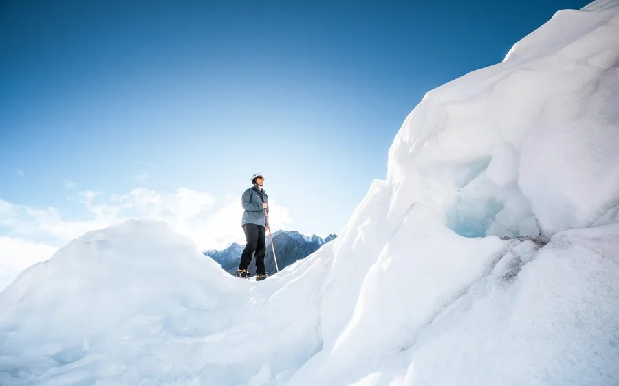 A hiker standing on an ice pinnacle high on the glacier in bright sun
