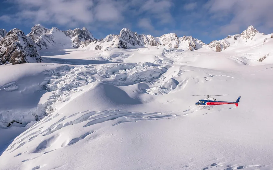 A helicopter parked on a wide snowfield below the Southern Alps