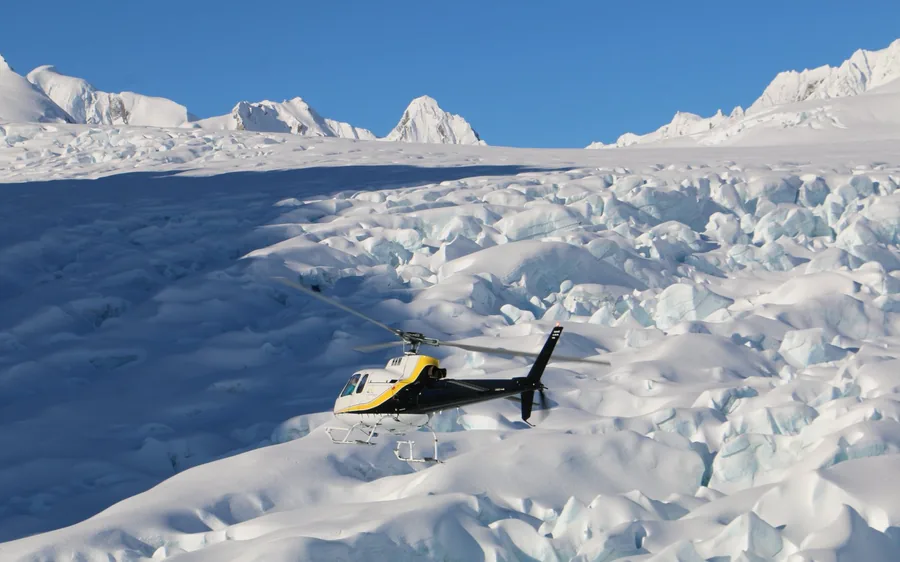 A yellow helicopter shut down on the snowfield above the glacier