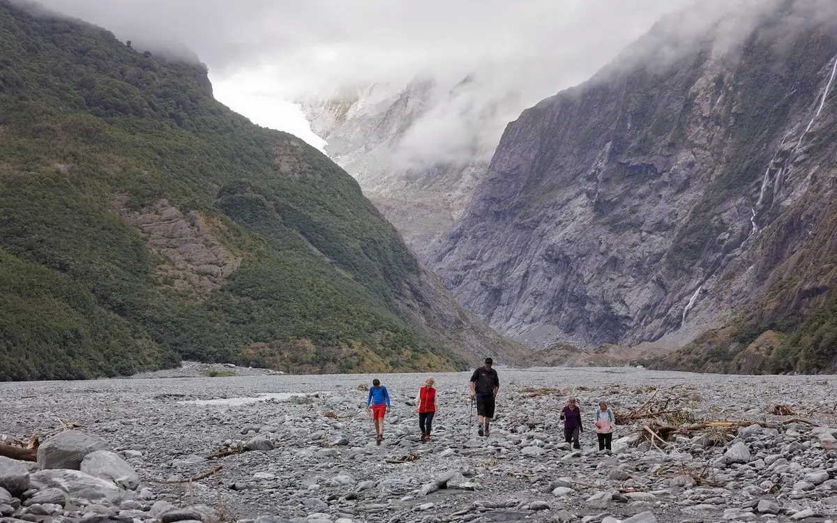 Walkers on the grey riverbed below Franz Josef Glacier